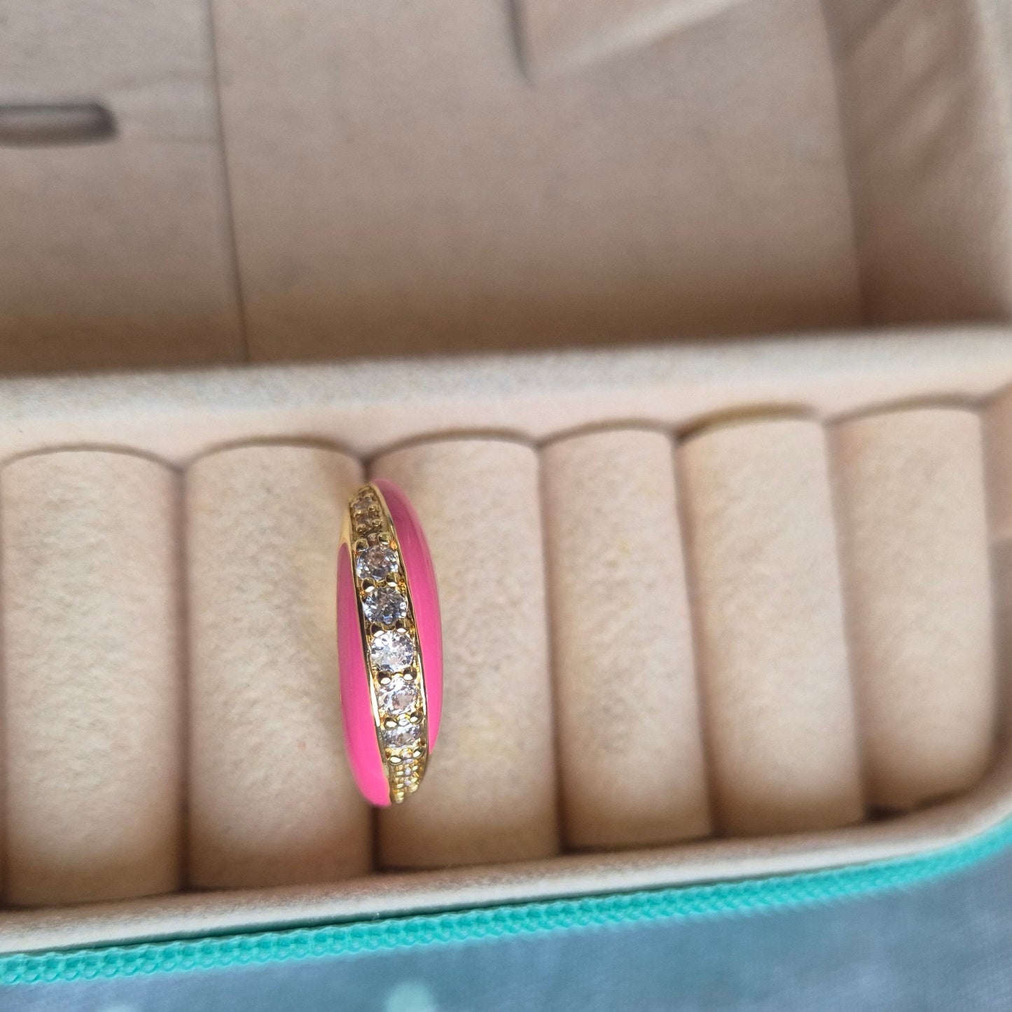 Pink ring with gold band and diamond accents on a jewelry case.