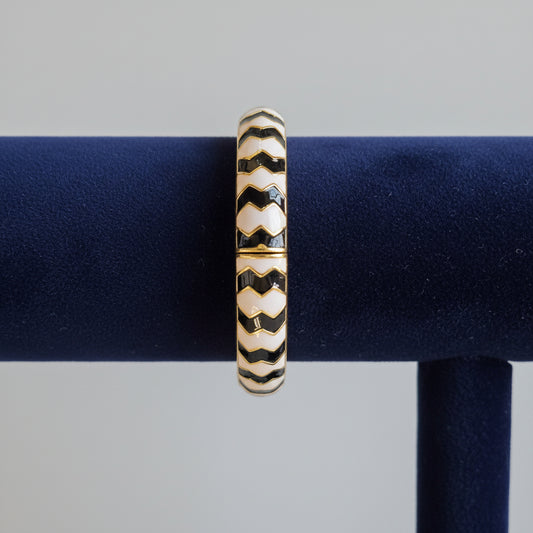 Gold bangle with black and white pattern on a blue and white checkered fabric background